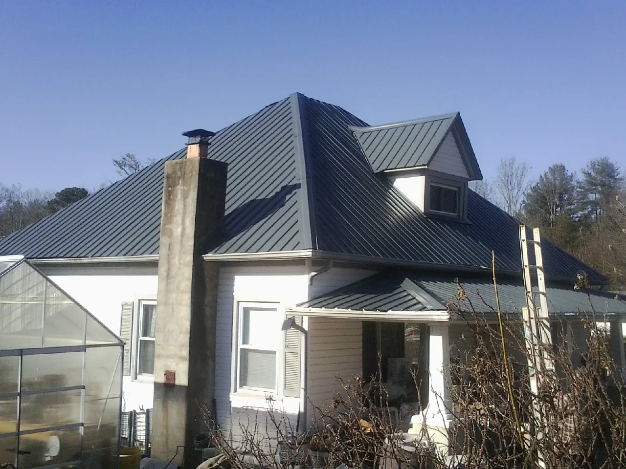 Dark blue standing seam metal roof on a white farmhouse with dormer — Slate & Tile Roof Repair by Roofing Brothers in Phillips