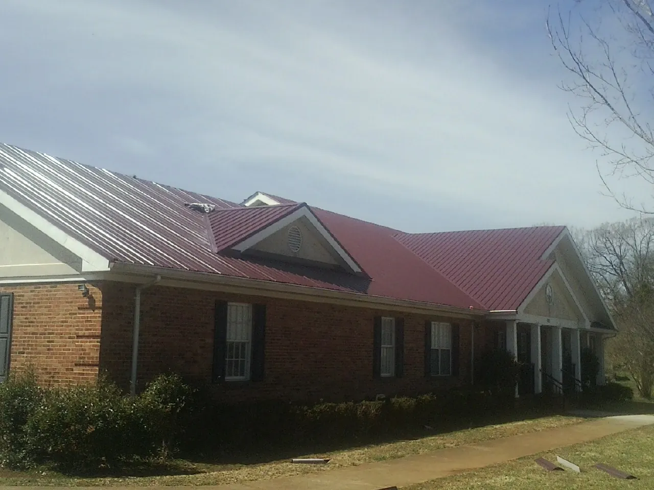 Red metal roof with gabled entries on a long brick building, from a Hail Damage Roof Repair job in Phillips