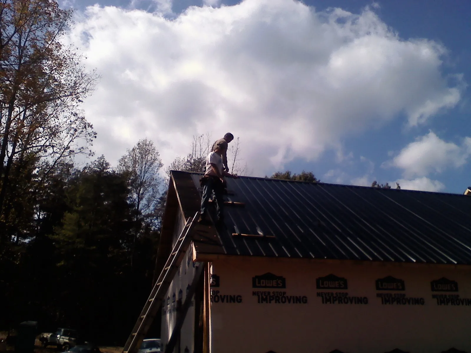Roofer fastening dark metal panels high against a cloudy sky, from a Roof Inspection job in Phillips
